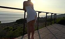 สาวใหญ่นมโตในชุดผ้าซาตินสีขาวมีส่วนร่วมในกิจกรรมทางเพศกลางแจ้งบนระเบียงในช่วงพระอาทิตย์ตกดิน